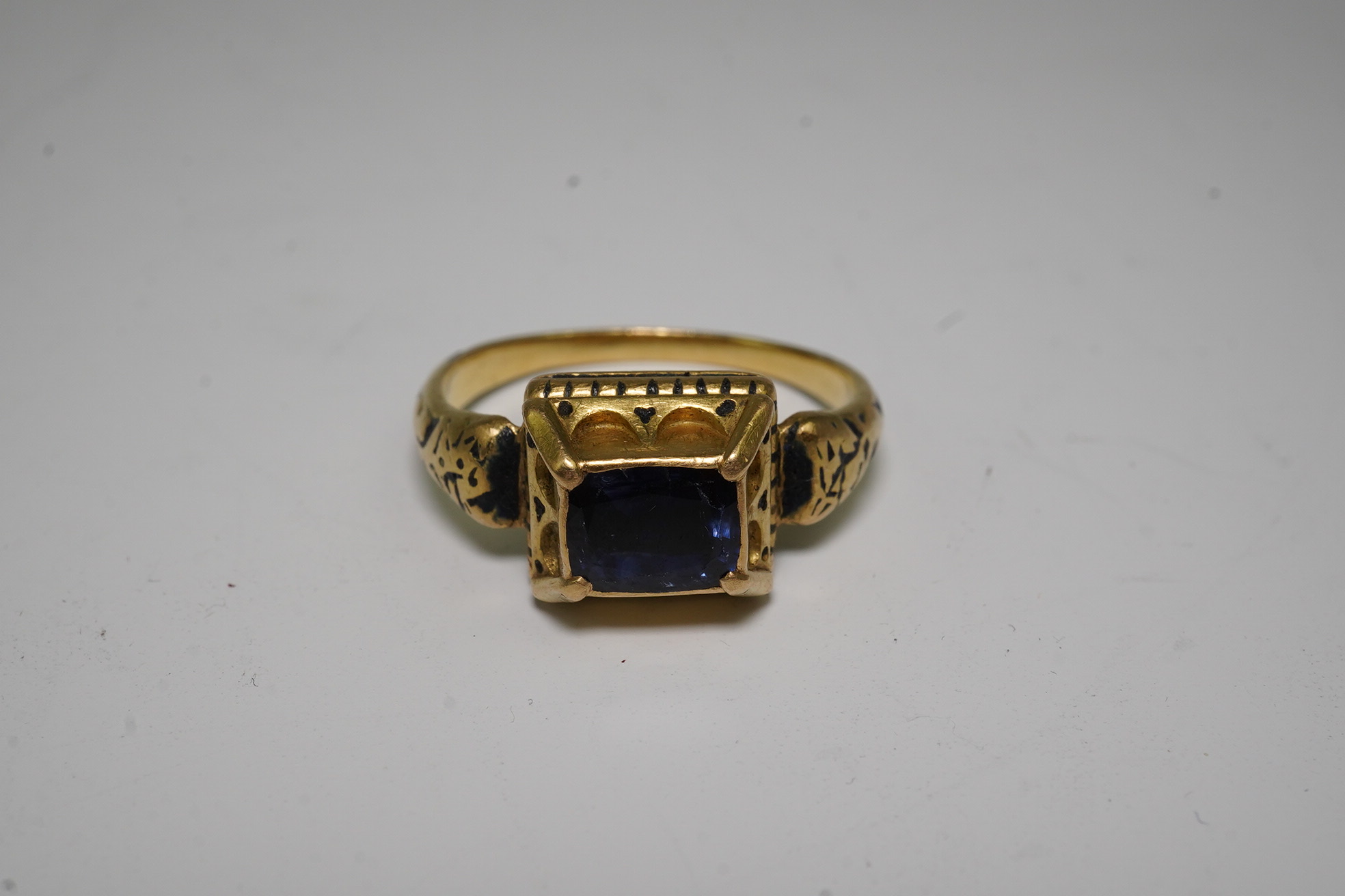 An antique high carat gold, black enamel and collet set cushion cut sapphire set 'poison' ring